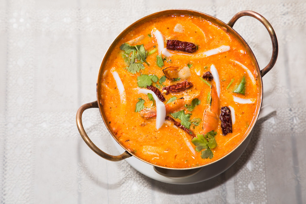 A top view shot of a creamy Tom Yum with dried chilis, cilantro, and what seems like calamari in a silver pot