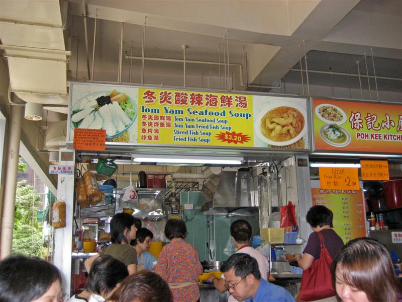 People sitting and eating in a canteen, also ordering at the store front of Tom Yum Seafood restaurant